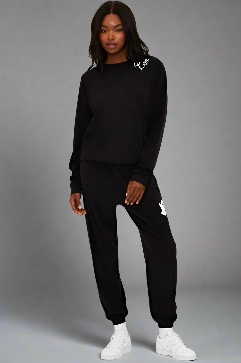 Person wearing a black tracksuit with brand logos on a white background