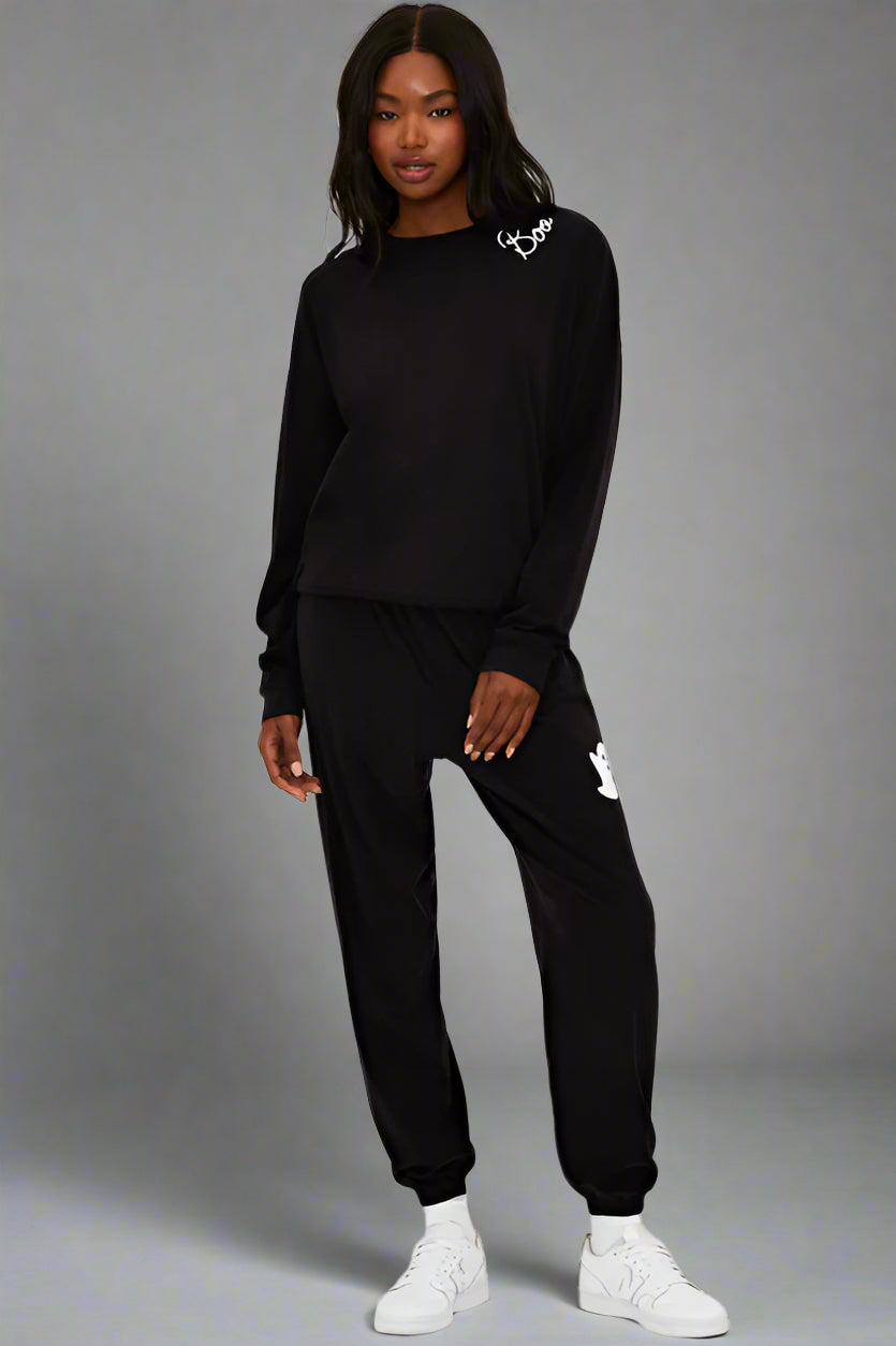 Person wearing a black tracksuit with brand logos on a white background