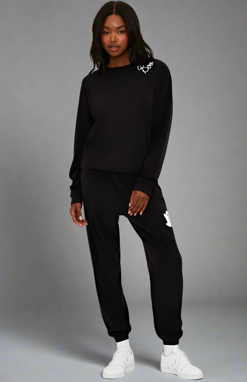 Person wearing a black tracksuit with brand logos on a white background