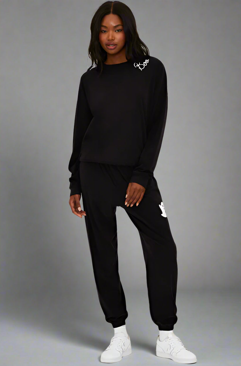 Person wearing a black tracksuit with brand logos on a white background