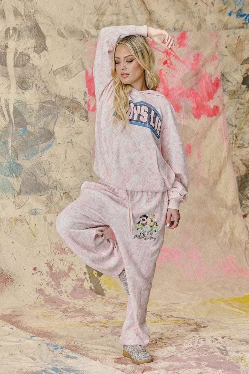 Woman in pink sweatshirt and pants posing against a textured wall with abstract designs.