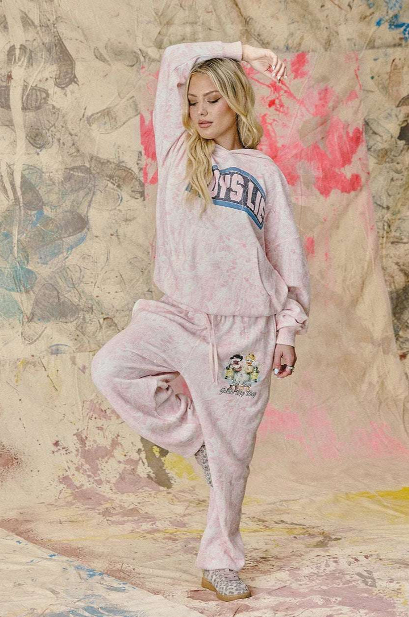 Woman in pink sweatshirt and pants posing against a textured wall with abstract designs.