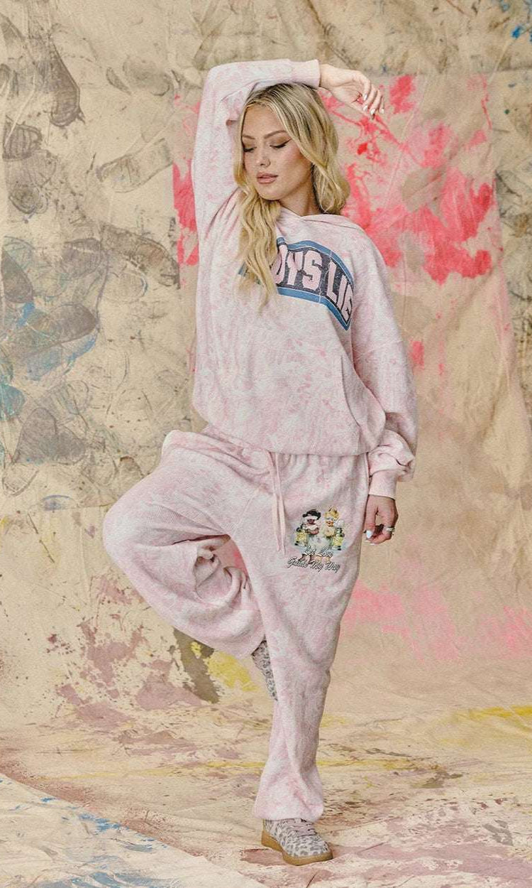 Woman in pink sweatshirt and pants posing against a textured wall with abstract designs.