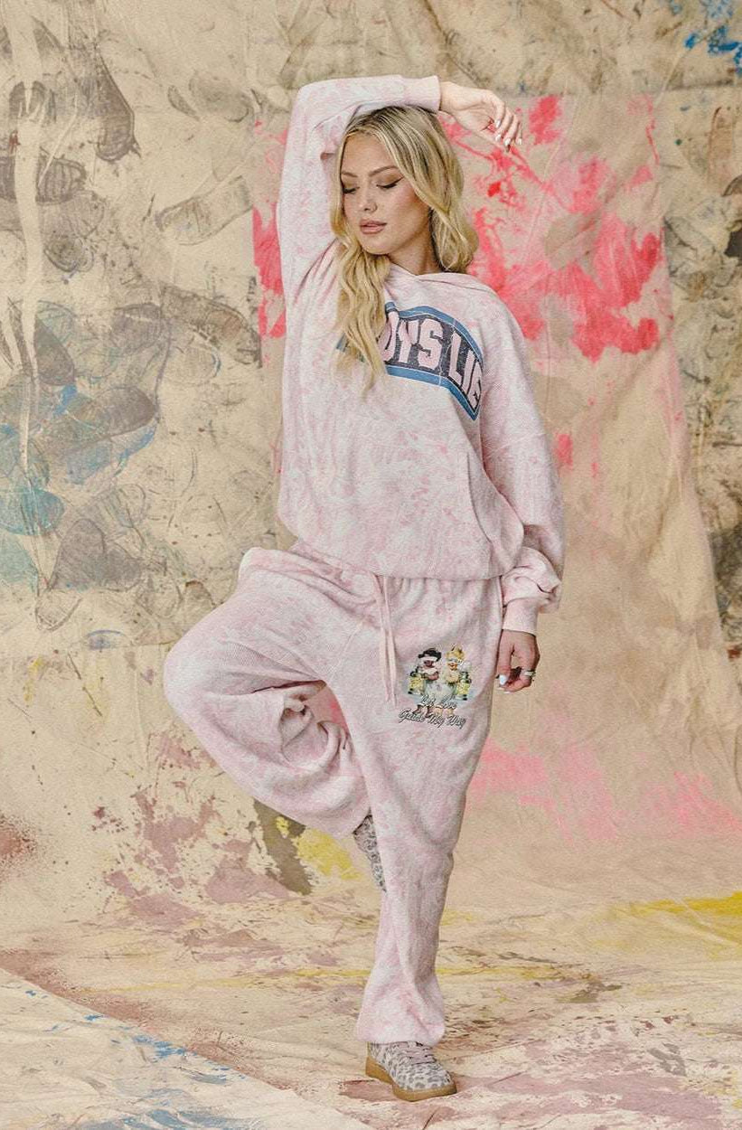 Woman in pink sweatshirt and pants posing against a textured wall with abstract designs.