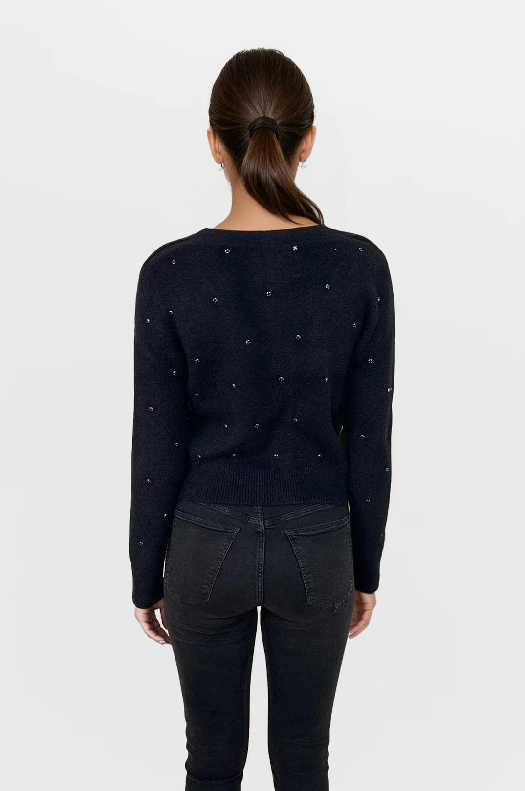 Person wearing a black sweater with small patterns and black pants on a white background