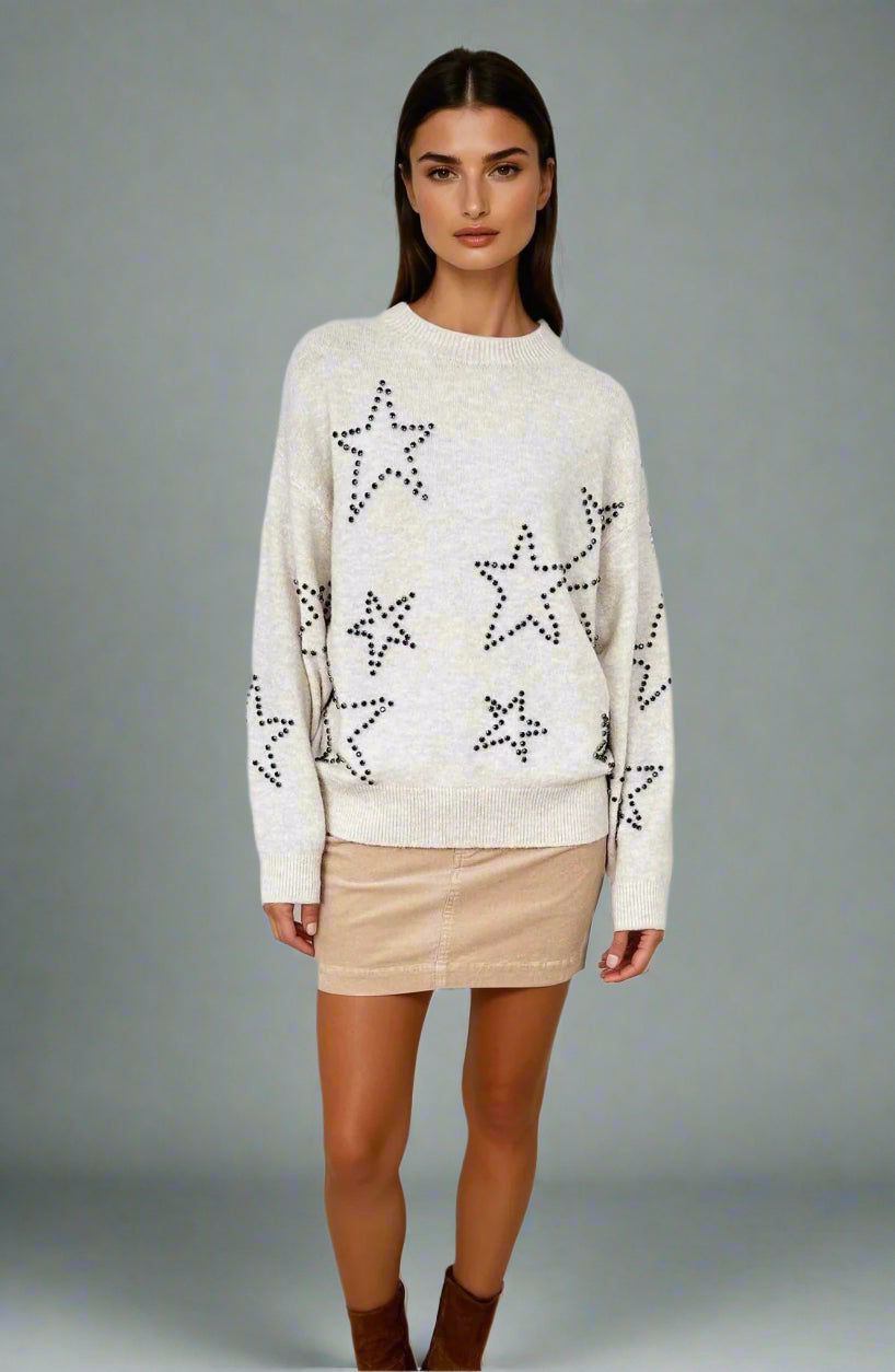 Woman wearing a cream sweater with star patterns on a white background