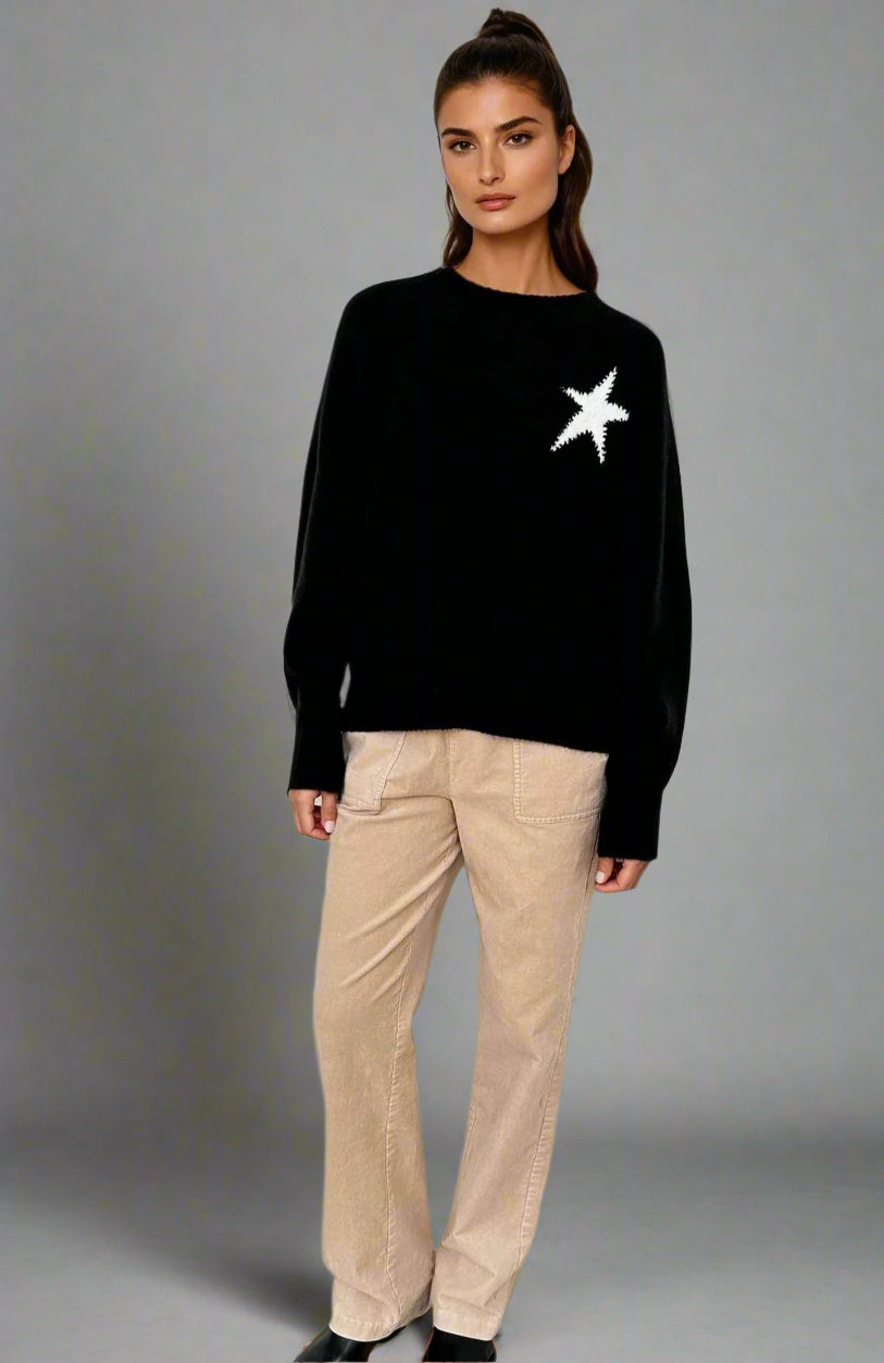 Woman wearing a black sweater with a white star design and beige pants on a white background