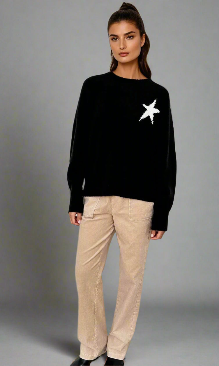Woman wearing a black sweater with a white star design and beige pants on a white background