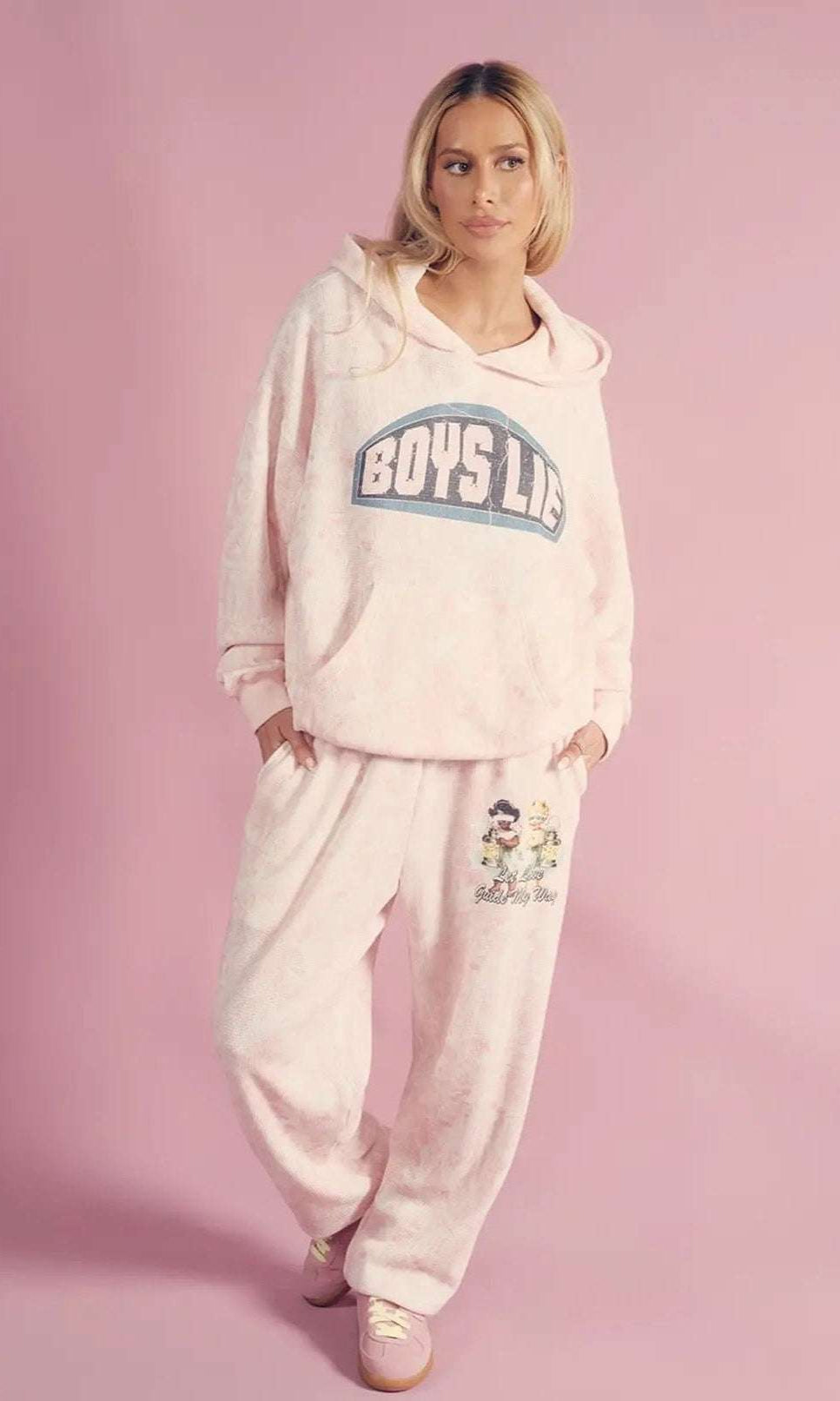 Person wearing a 'Boys Lie' hoodie and pants on a pink background