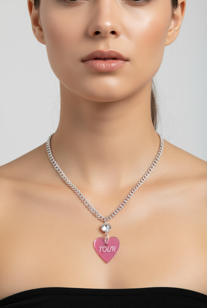 Woman wearing a silver necklace with a pink heart-shaped pendant labeled 'TOUR' on a plain background
