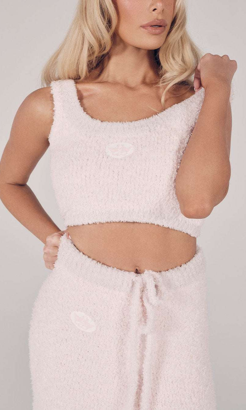 Woman wearing a light pink textured top and pants against a plain background