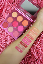 Makeup palette with color swatches on a pink textured background