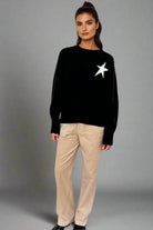 Woman wearing a black sweater with a white star design and beige pants on a white background
