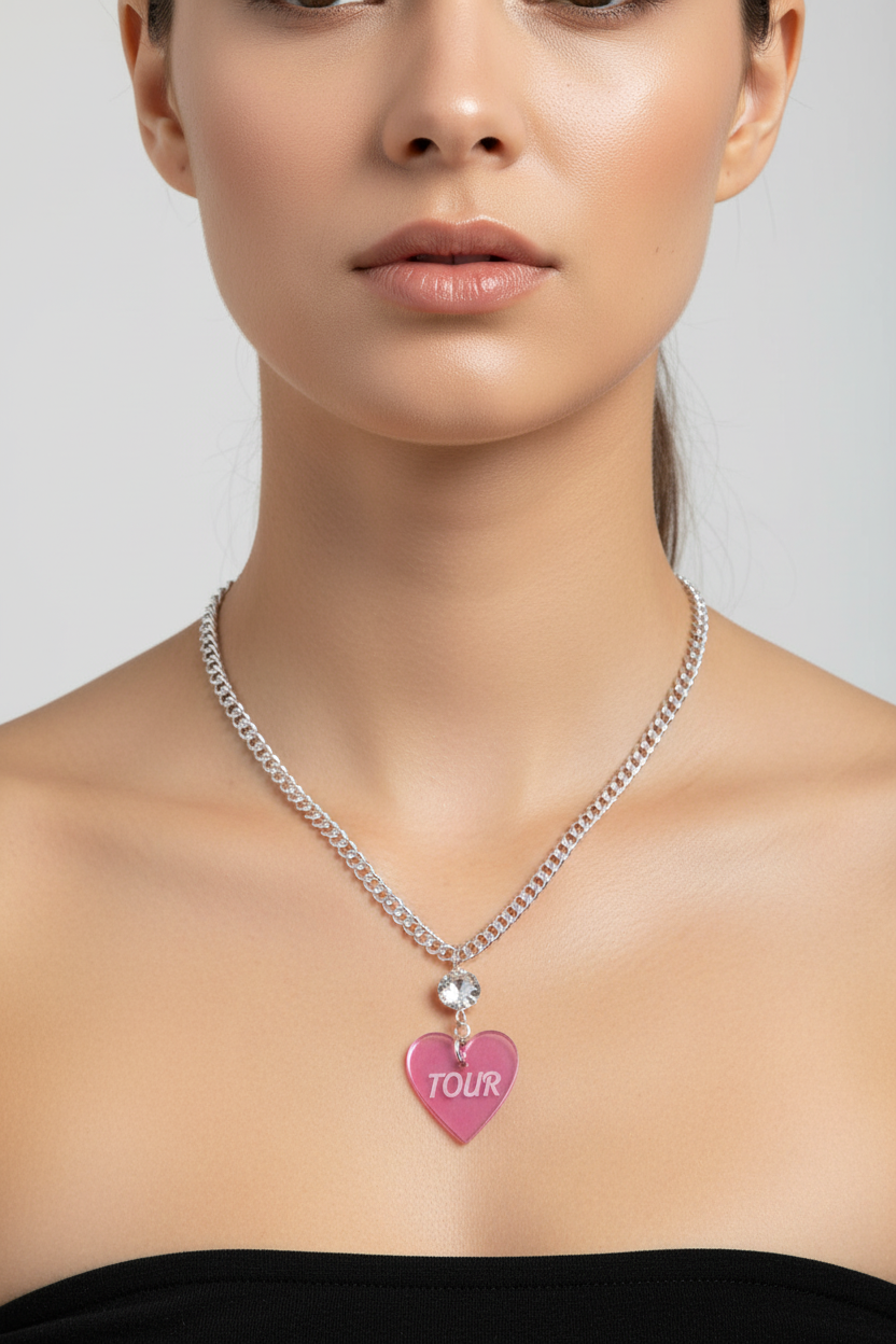 Woman wearing a silver necklace with a pink heart-shaped pendant labeled 'TOUR' on a plain background